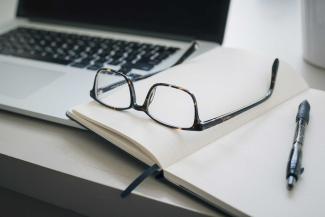 Glasses on a notebook, next to a laptop.
